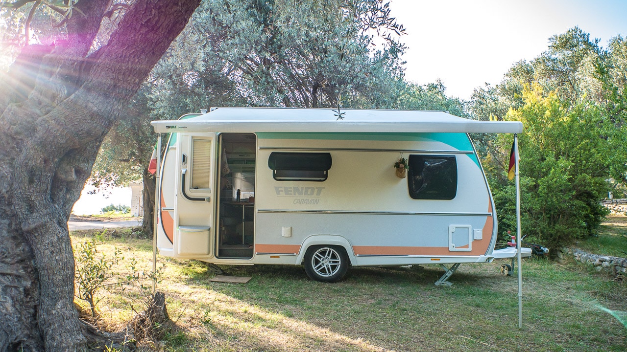 Camping mit Wohnwagen auf einer Wiese unter einem Baum